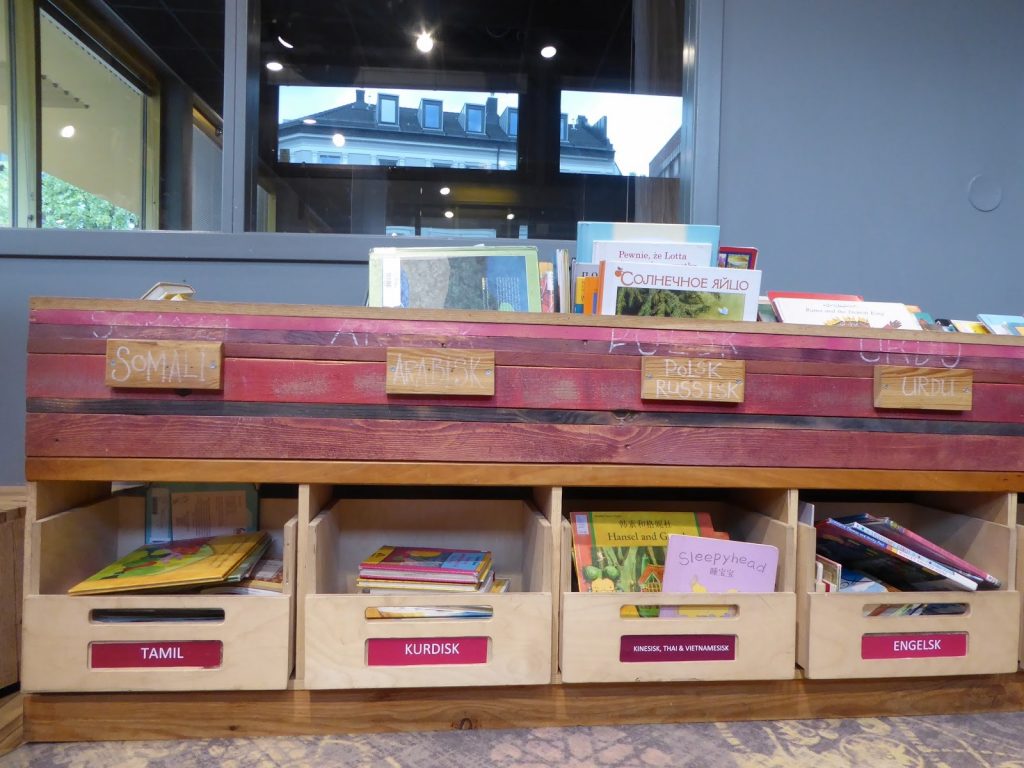 Vue sur les albums en langues étrangères situés dans des bacs en bois de récup à la bibliothèque tous publics de Tøyen.