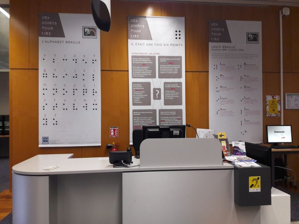 Photographie d'une banque d'accueil avec derrière des bannières sur l'histoire du braille