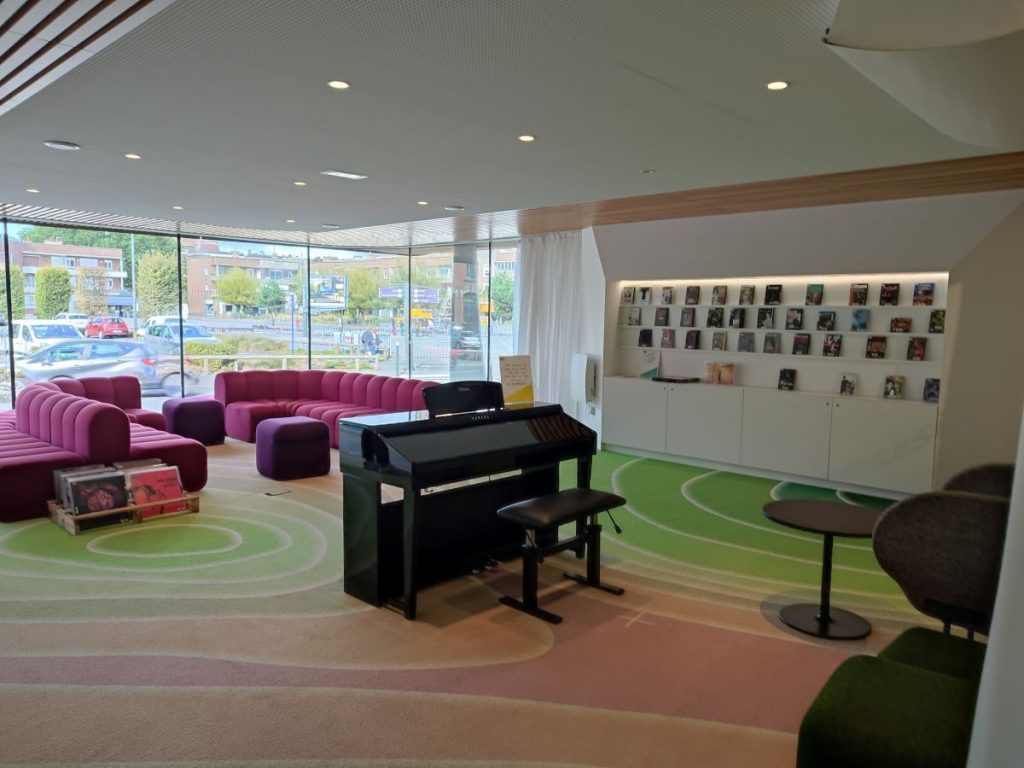 Photo du salon de musique de la B!b de Dunkerque avec son piano au centre et des canapés rouges autour