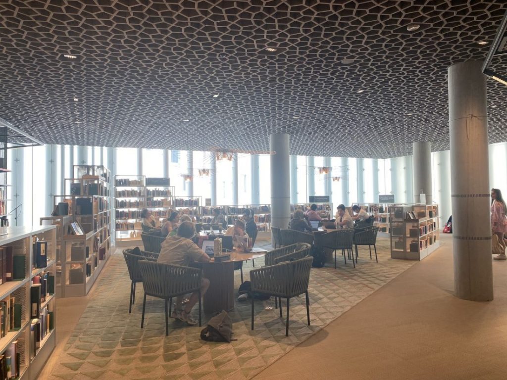 Espace intérieur de la Deichman Bjorvika Bibliotek : des étagères de hauteur variées entourent quelques tables entourée de chaises confortables qui accueillent de nombreux lecteurs © Bpi