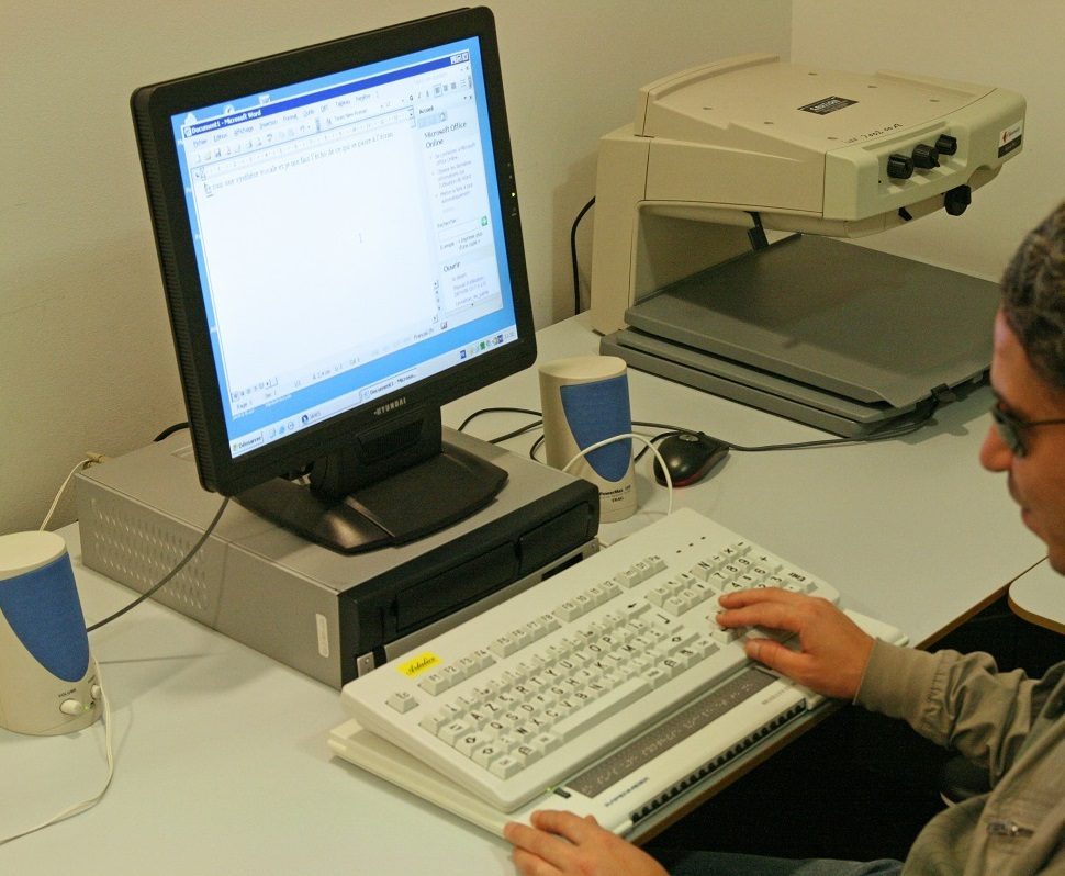 Une personne en situation de handicap visuel utilise un ordinateur et la plage braille dans une loge.