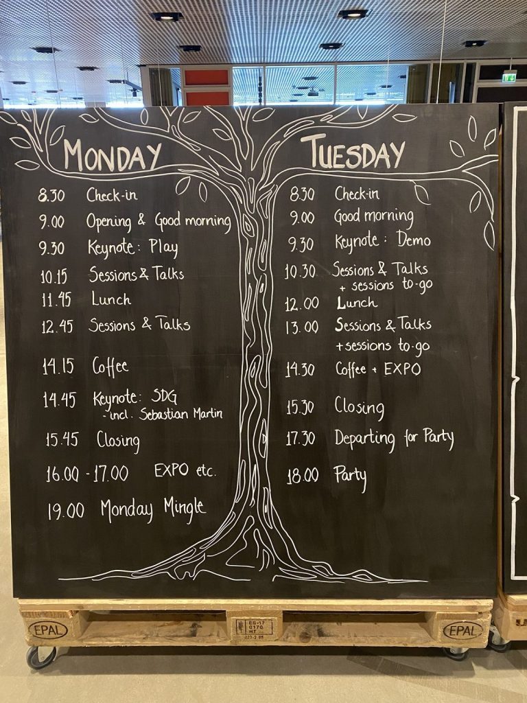 Tableau noir avec tout le programme du festival écrit à la main autour d'un arbre dessiné