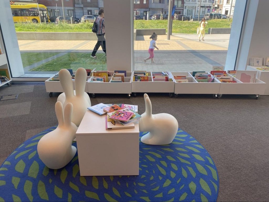 Espace jeunesse de la bibliothèque comportant des bacs à albums devant une baie vitrée et du mobilier blanc en forme de lapins.