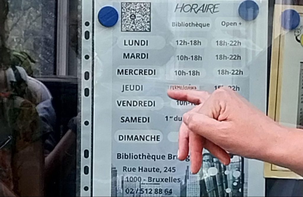 Un doigt pointe l’affichage des horaires d’ouverture de la bibliothèque Bruegel à Bruxelles.