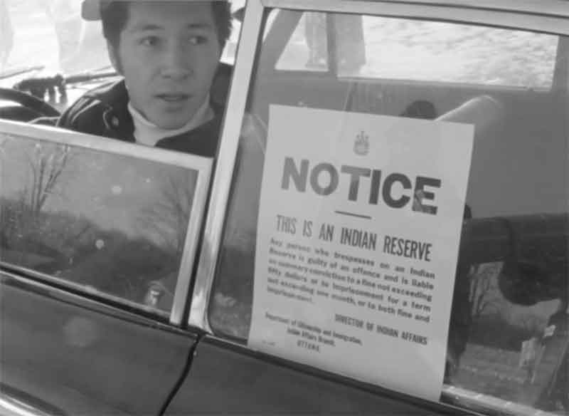 Un homme dans une voiture et une affiche qui prévient qu'il est sur une réserve indienne.