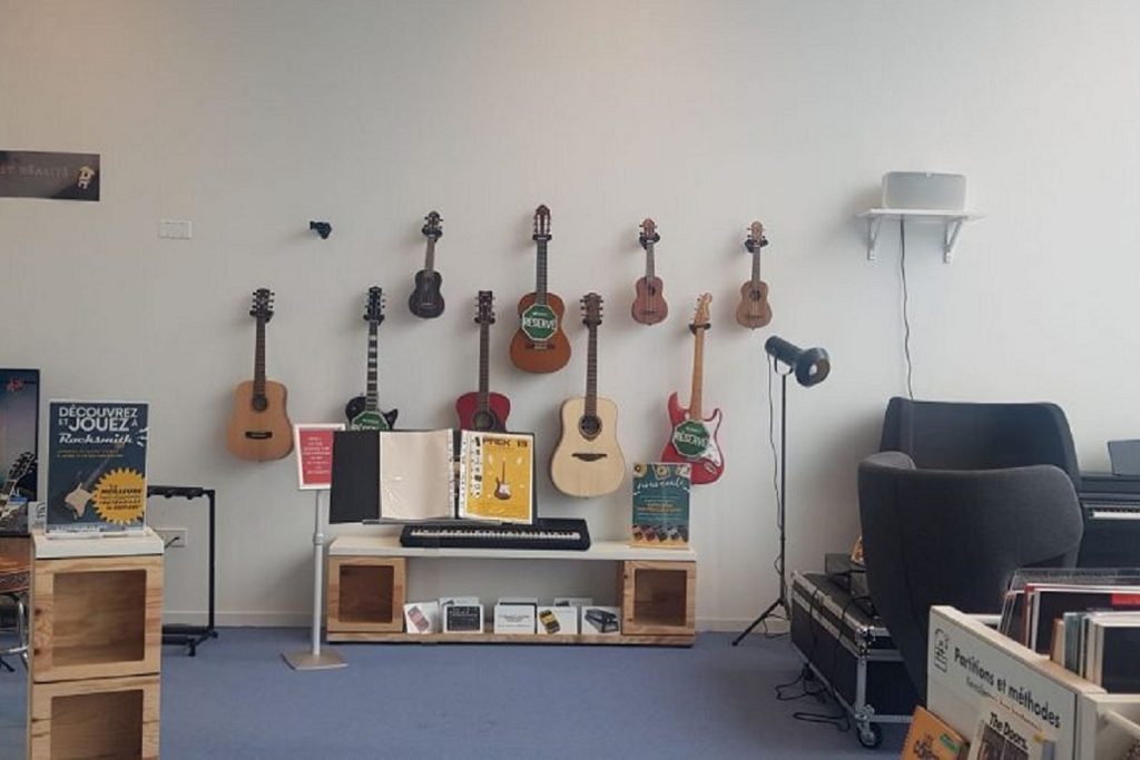 Mur des instruments de la médiathèque : guitares, ukulélés et clavier suspendus et exposés, disponibles au prêt.