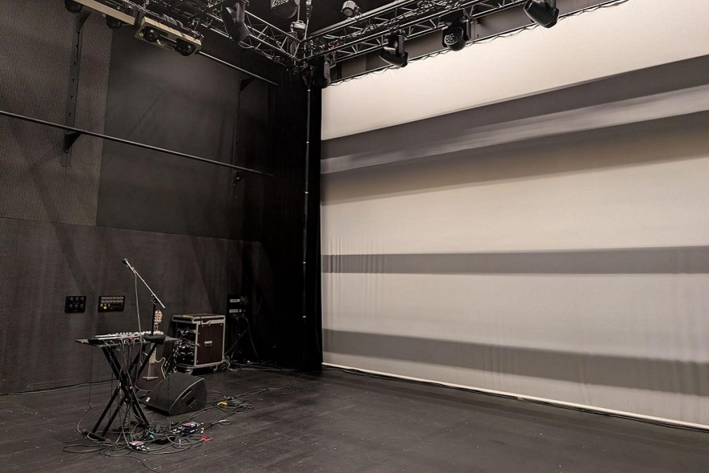 Salle de concert de la SMAC aux murs noirs, avec instruments et matériel de sonorisation installés sur scène.