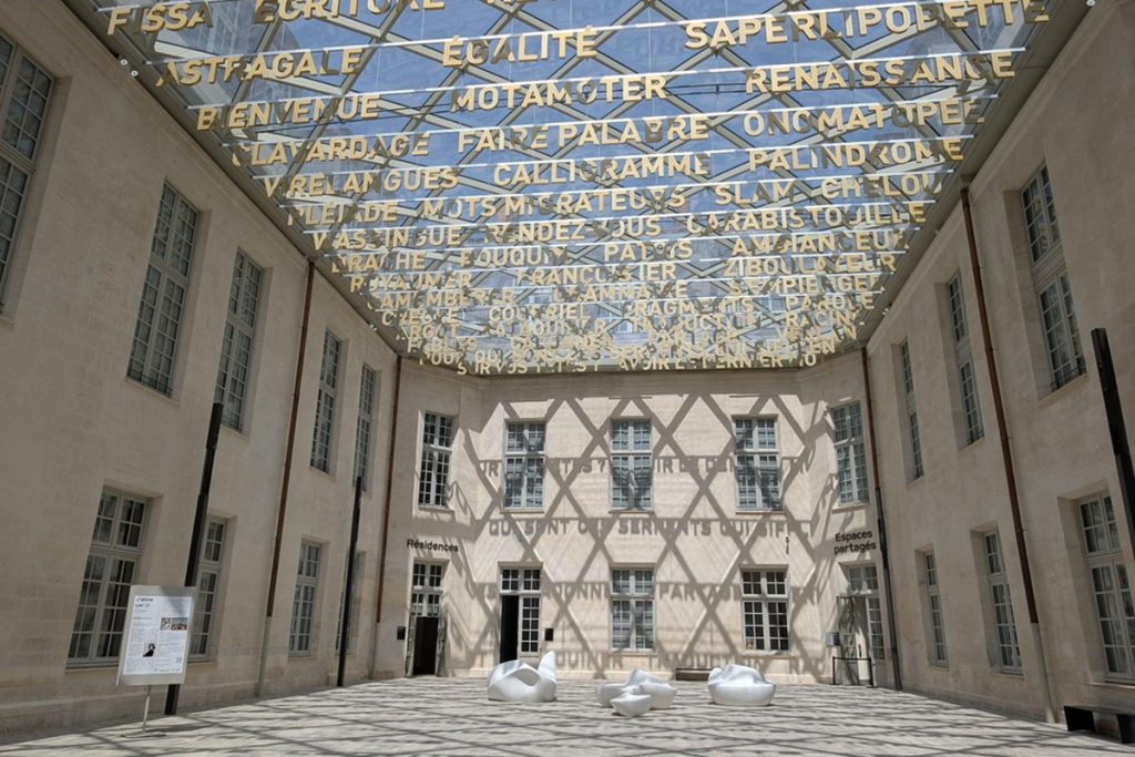 Cour intérieure de la Cité internationale de la langue française, surmontée d'une verrière portant en lettres dorées des mots issus de la langue française (argot, néologismes, francophonie).