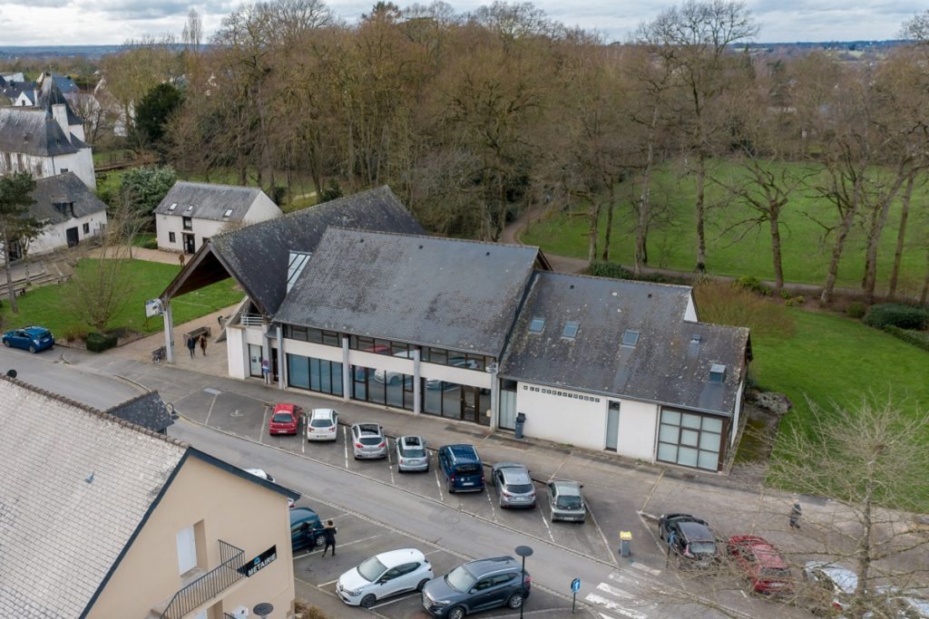 Vue aérienne de l'ancienne médiathèque de Pacé, bâtiment à toiture d'ardoise entouré d'un parking et d'un parc arboré.