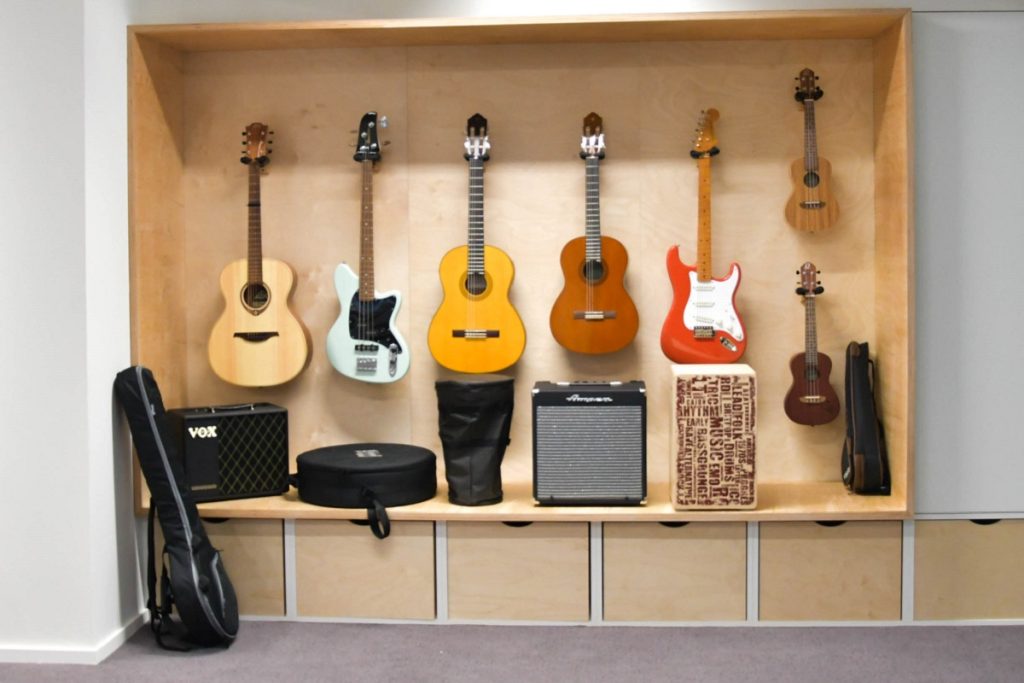Niche murale en bois présentant des instruments à emprunter : guitares, basse, ukulélés et amplificateurs.