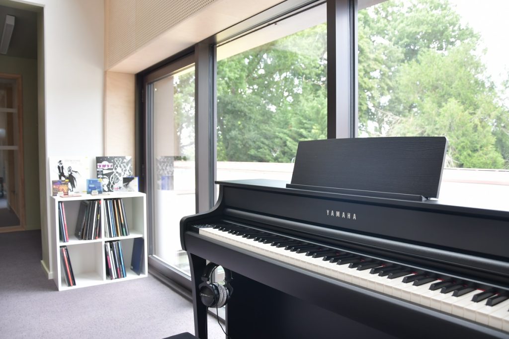 Piano numérique Yamaha installé près d'une baie vitrée, à côté d'un bac de vinyles, dans l'espace musique.