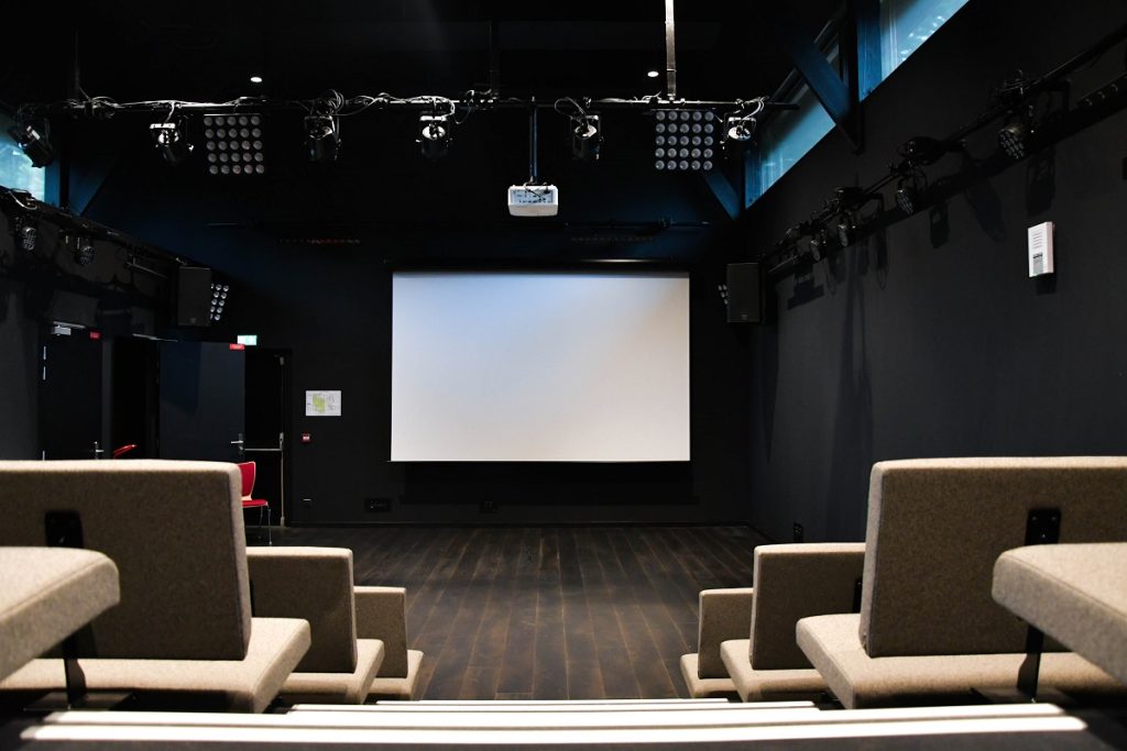 Salle d'animation aux murs noirs équipés d'éclairages et de sonorisation, avec sièges face à un écran de projection.