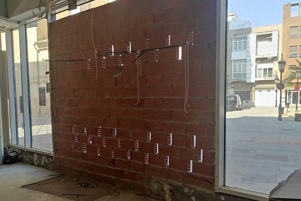 Entrée de la bibliothèque de Paiporta en cours de sécurisation après l'inondation : mur en briques renforcé de dispositifs métalliques, vitrines encore vides.