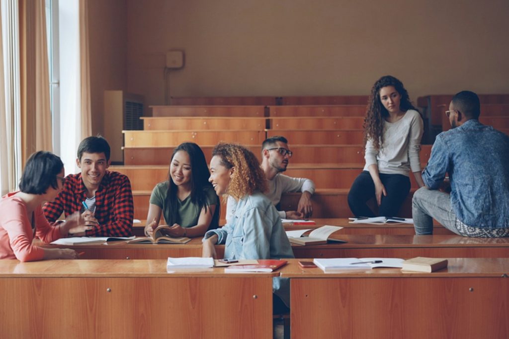 Étudiants échangeant en petits groupes dans un amphithéâtre, assis sur les gradins en bois.