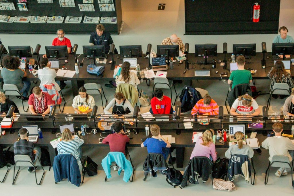 Vue plongeante sur des étudiants travaillant sur ordinateurs portables, installés en rangées dans un espace de bibliothèque universitaire.
