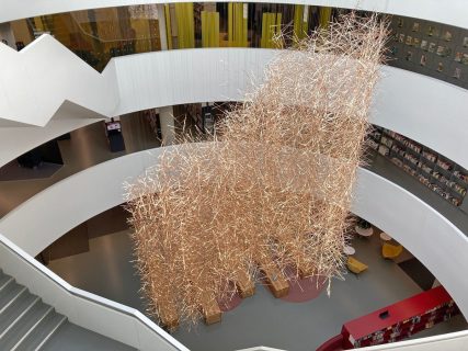 Au centre d'un escalier circulaire, une grande scuplture est suspendue et forme comme un pluie métallique dorée