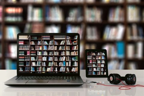 Un ordinateur et une tablette sont posés devant une bibliothèque, leurs écrans montrent des étagères de livres.