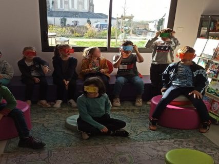 Enfants assis portant des lunettes pour voir différemment lors d'une animation dans une bibliothèque.