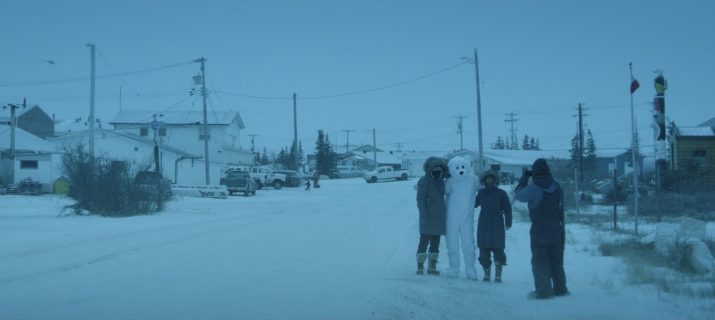 Photogramme du film Churchill, la ville des ours polaires montrant plusieurs personnes posant aux côtés d'une autre déguisée en ours polaire, dans une rue enneigée.