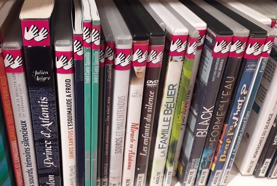 Étagère de DVD étiquetés avec le pictogramme fushia représentant le handicap auditif - LSF