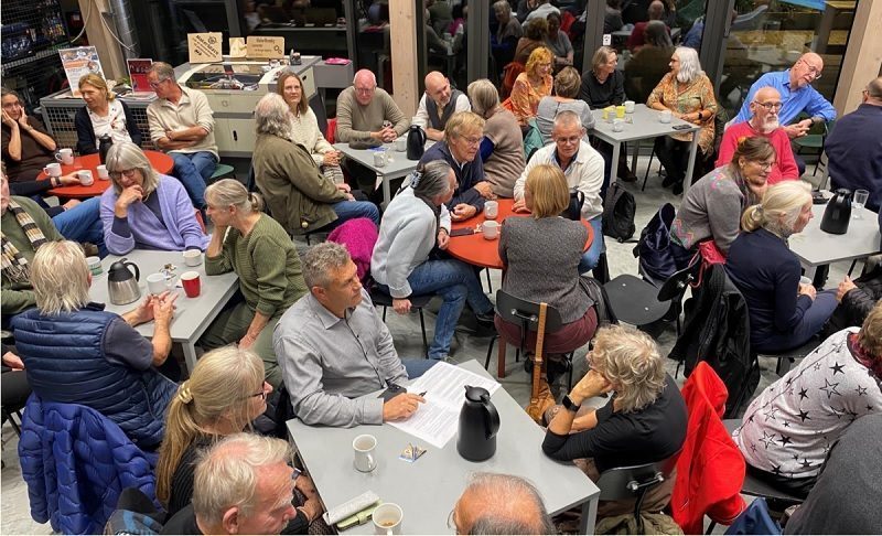 Plusieurs groupes de personnes sont attablées pour assister à un débat dans la bibliothèque